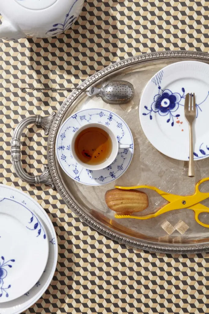 Table top shot of a tea set showing a cup, small plate, tea pot, tea egg, 2 pieces of sugar, a cookie