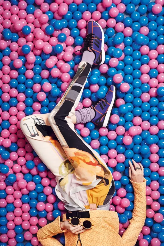 Top view, the lower body part of a female model with patterned trainers, matching sneakers, holding sunglasses in her hand