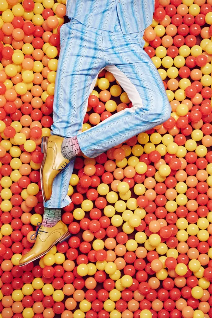 top view, a male model surrounded by plastic balls with patterned pants and leather shoes
